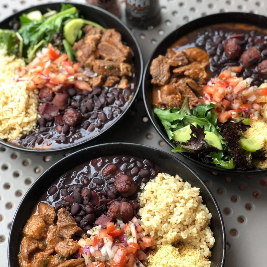 Three Prato Feito plates with black bean stew, beef, cassava flour, vinaigrette and salad