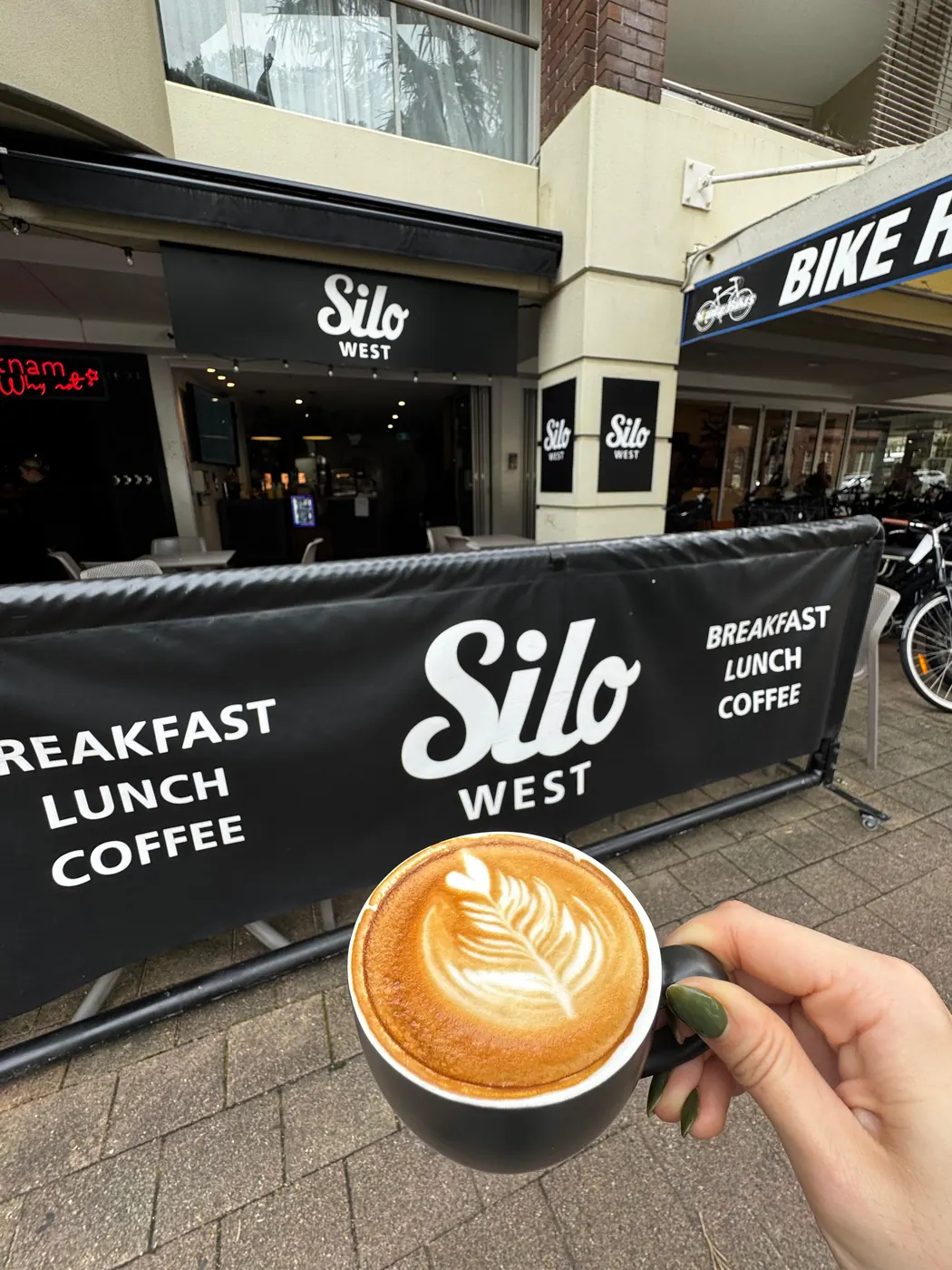 A flat white held up in front of the Silo West banner