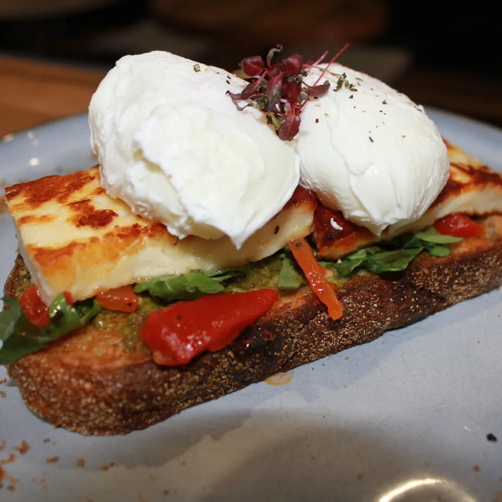 Two poached eggs on grilled halloumi, chargrilled capsicum, pesto and rocket on toasted sourdough