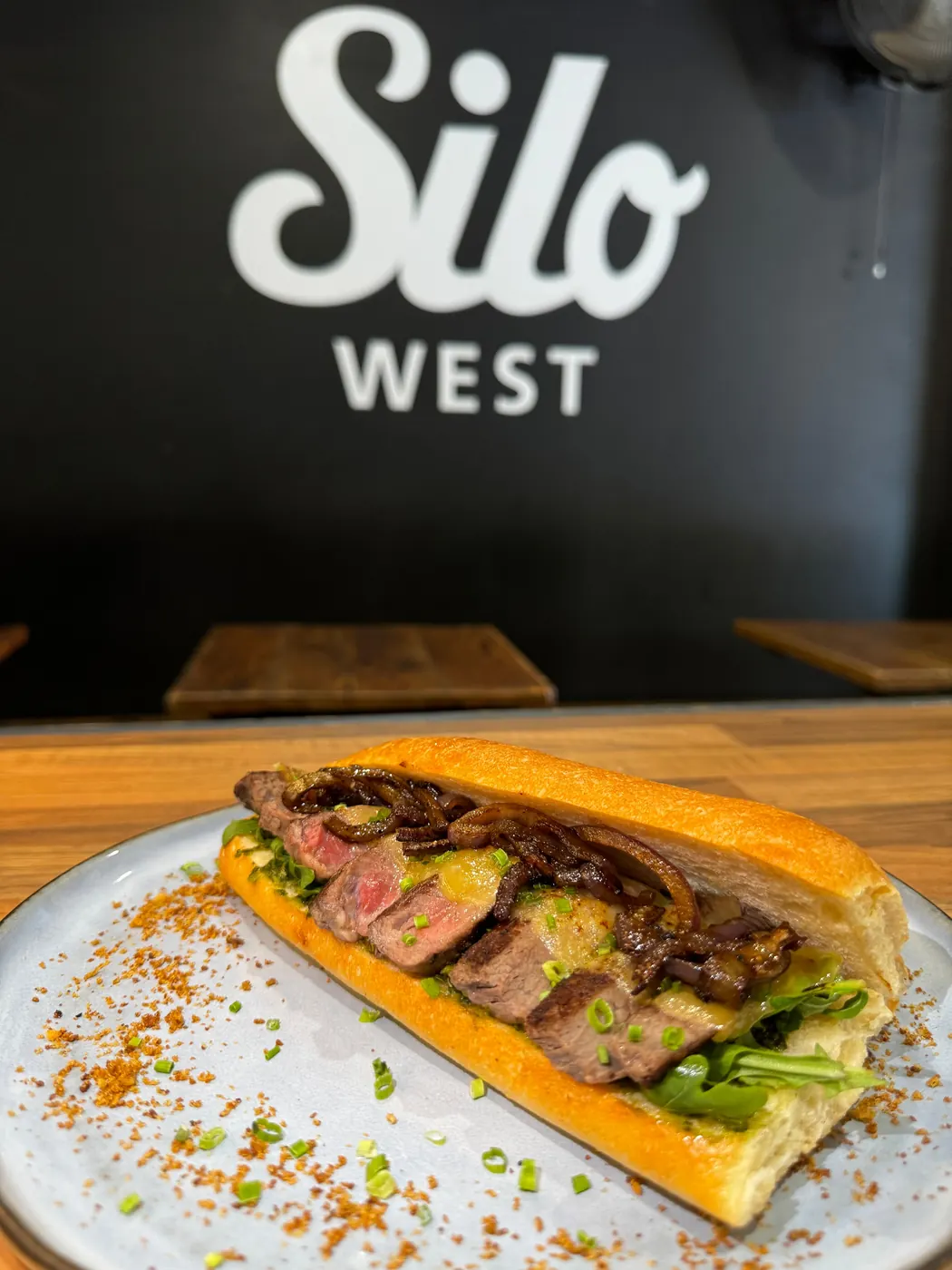 A steak sandwich on a table inside Silo West, under the Silo West sign